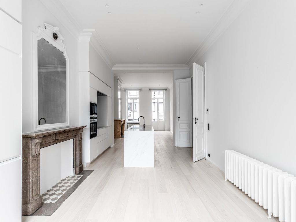 Salon moderne avec cuisine blanche lumineuse, miroir orné, style épuré et détails classiques élégants.