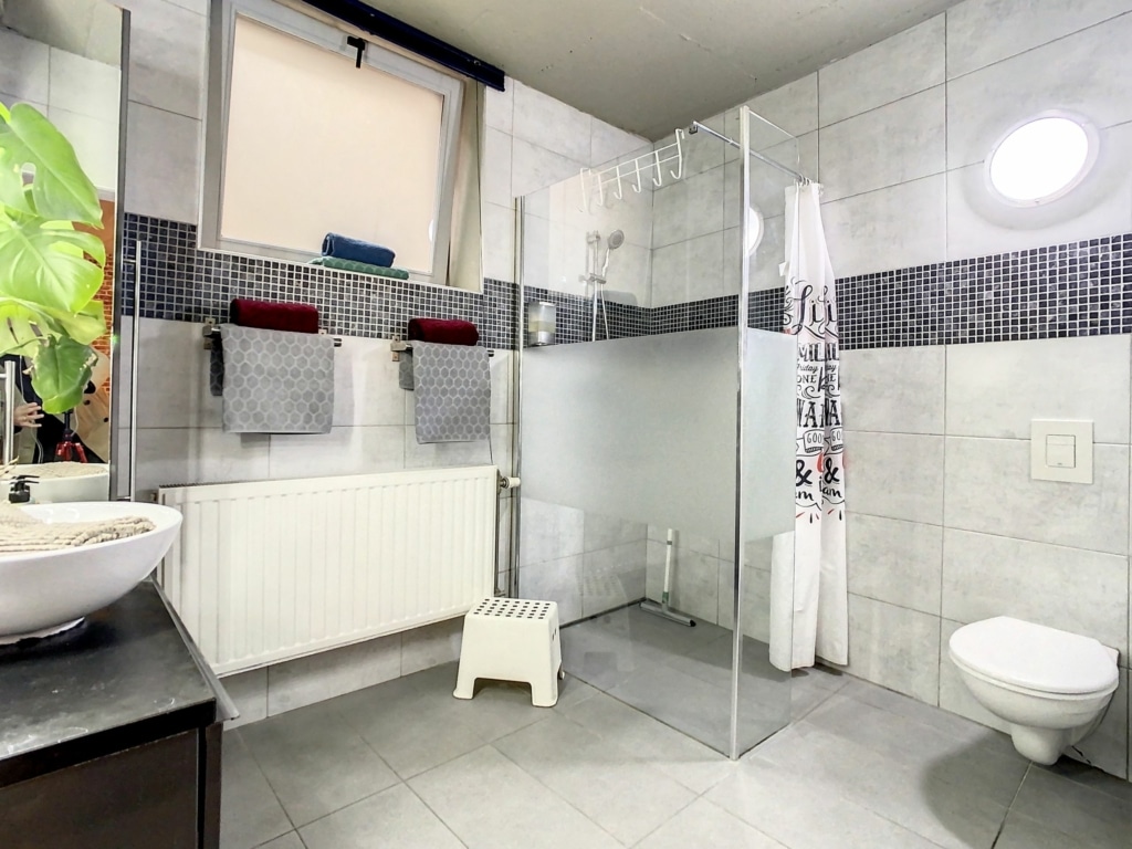 Salle de bain moderne minimaliste avec douche en verre, lavabo élégant et touches de couleur.