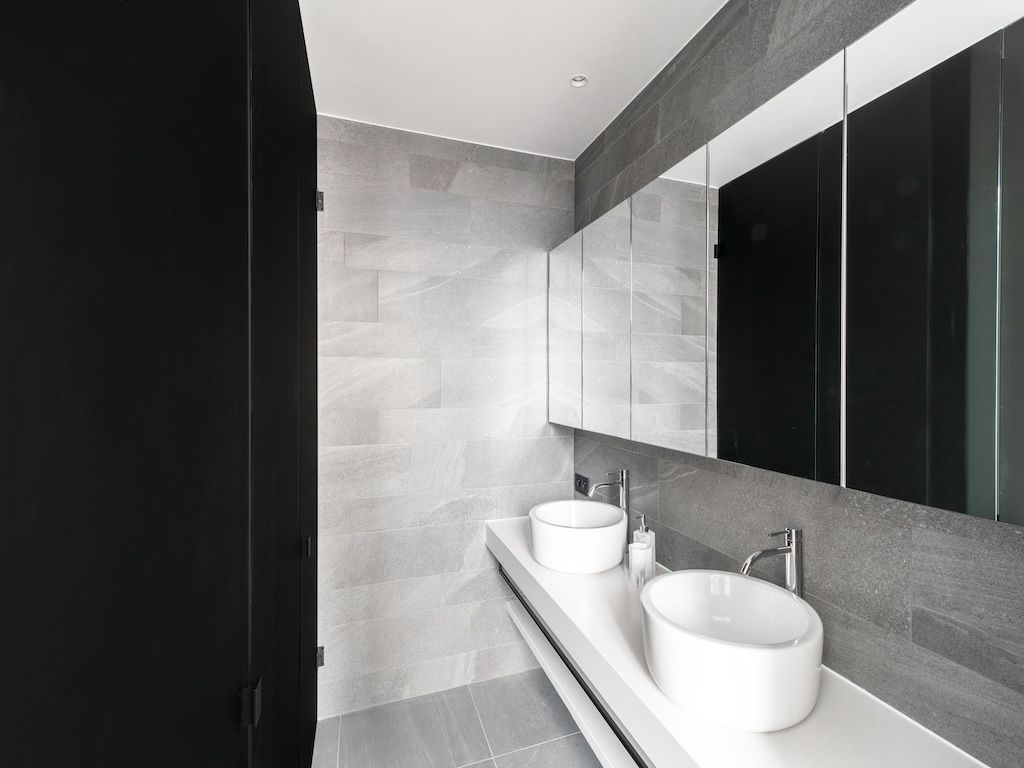 Salle de bain minimaliste avec vasques rondes, miroirs intégrés et contraste porte sombre élégante.