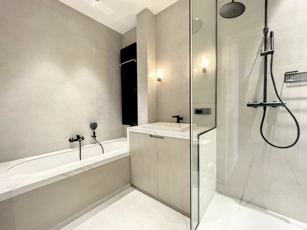 Salle de bain minimaliste en gris clair avec baignoire, douche en verre et accents noirs modernes.