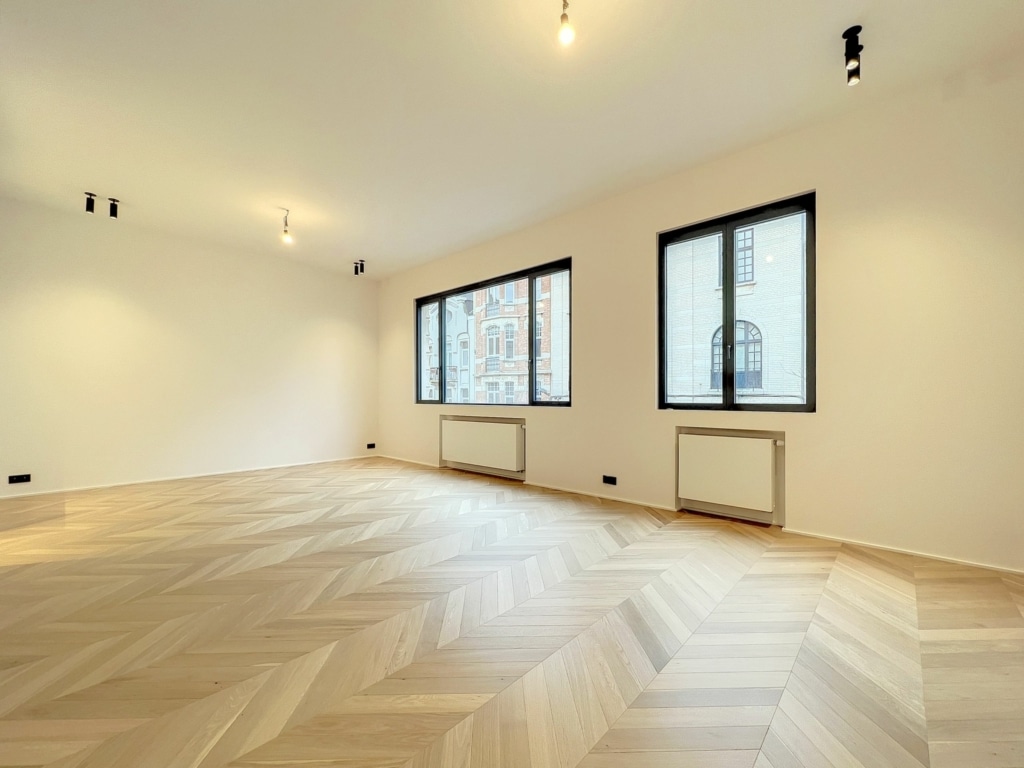 Salle moderne lumineuse avec parquet en chevrons, grande fenêtres et ambiance épurée.