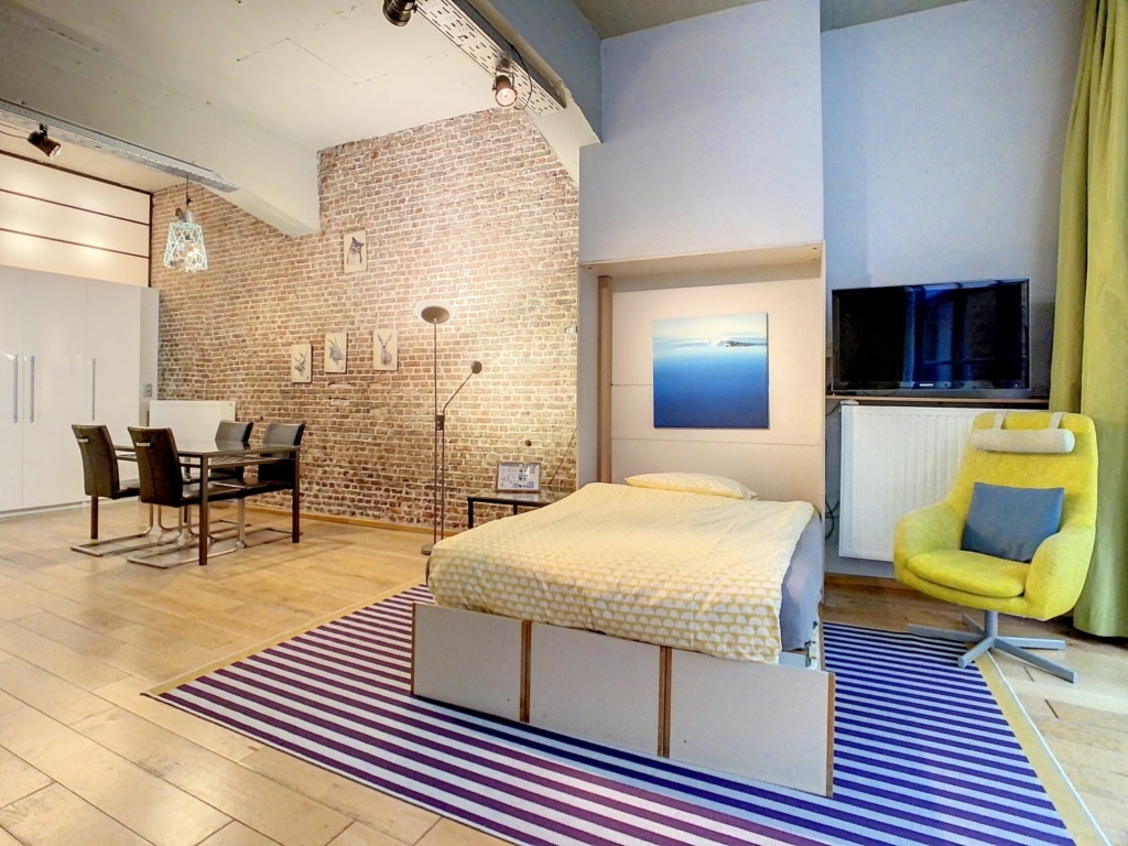 Studio moderne avec mur en brique, mobilier industriel, espace cosy et lumineux.