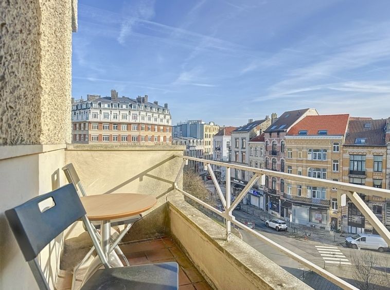 Balcon charmant sur une rue urbaine animée avec bâtiments variés et ciel bleu.