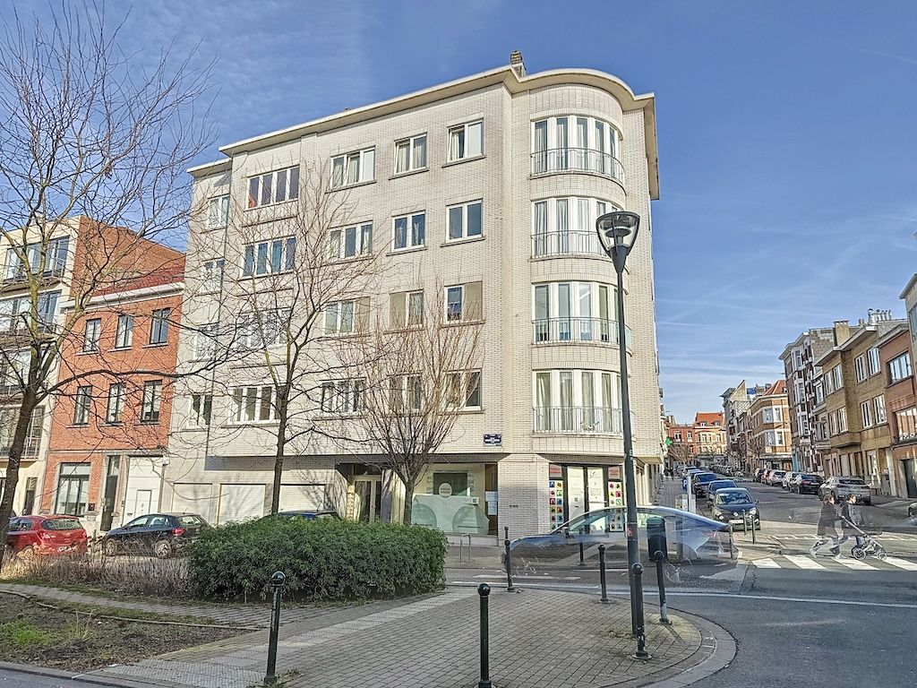 Bâtiment moderne au coin dune rue, avec façades claires, grandes fenêtres et espace vert urbaine.