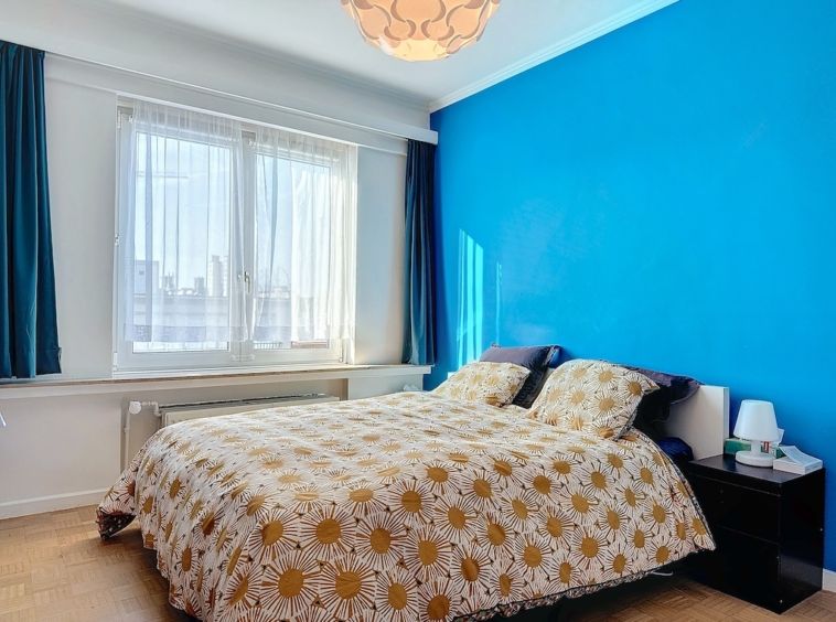 Chambre moderne, mur bleu vif, lit à motifs de tournesols, éclairage naturel, ambiance accueillante.