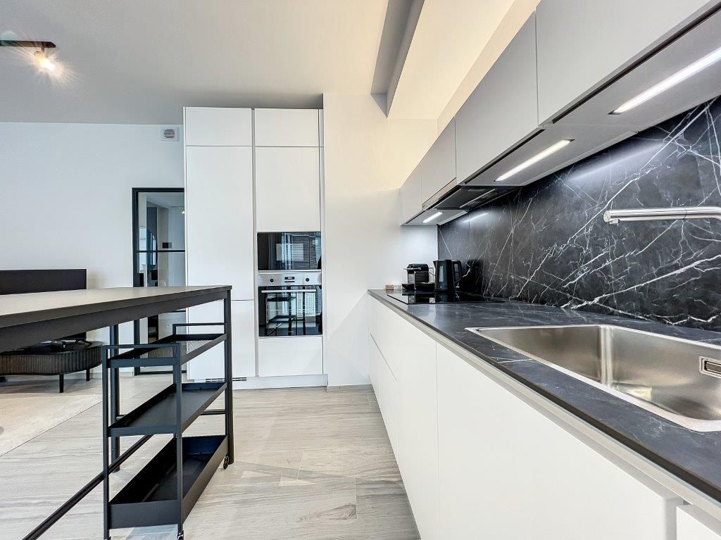 Cuisine moderne épurée avec plan de travail en granit noir, murs en marbre et espace repas lumineux