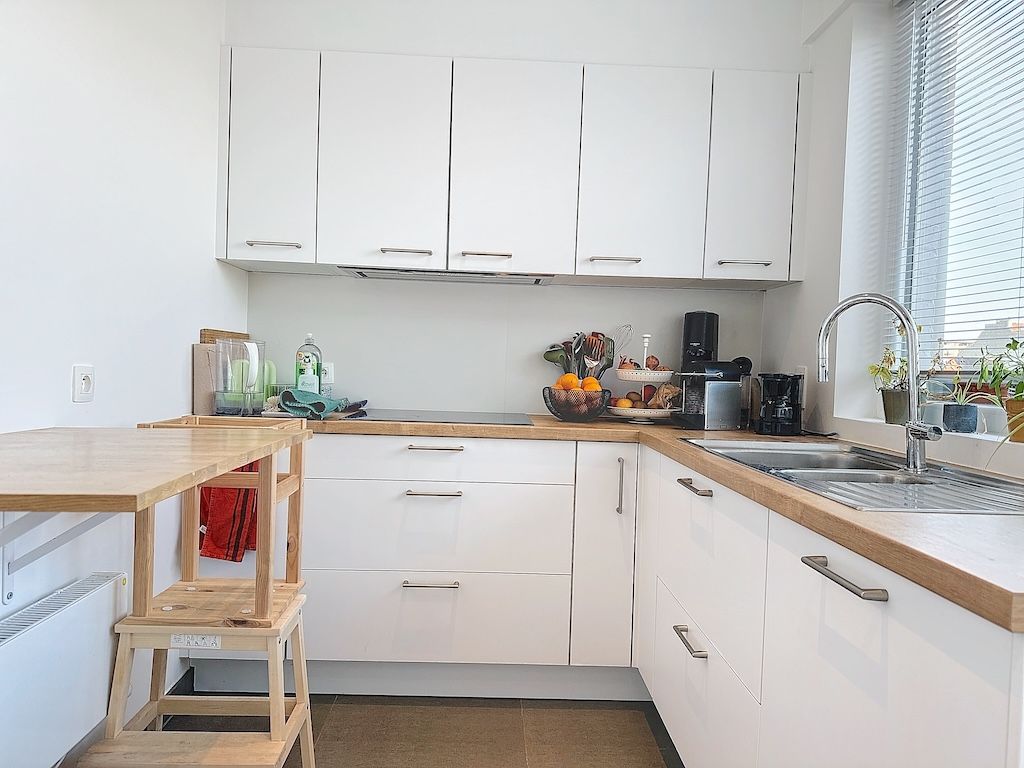 Cuisine moderne lumineuse avec mobilier blanc, détails en bois et espace repas naturel.