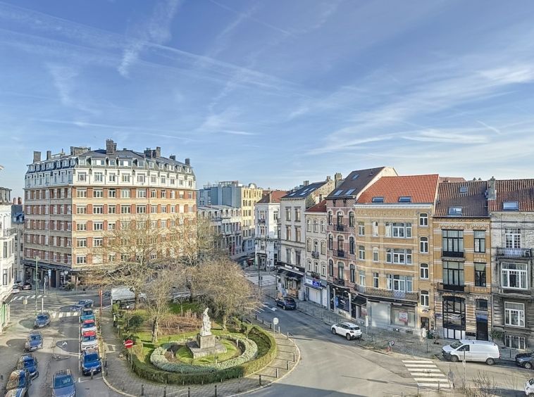 Quartier pittoresque avec parc, fontaine, architecture variée, rue animée et ciel bleu.