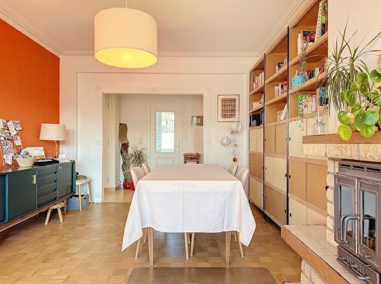 Salle à manger moderne avec mur orange, table blanche, luminaires contemporains et décor végétal.