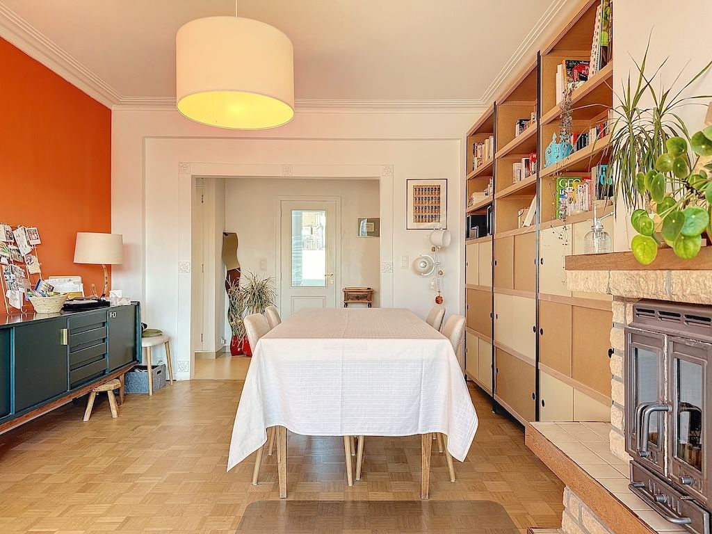 Salle à manger moderne avec mur orange, table blanche, luminaires contemporains et décor végétal.