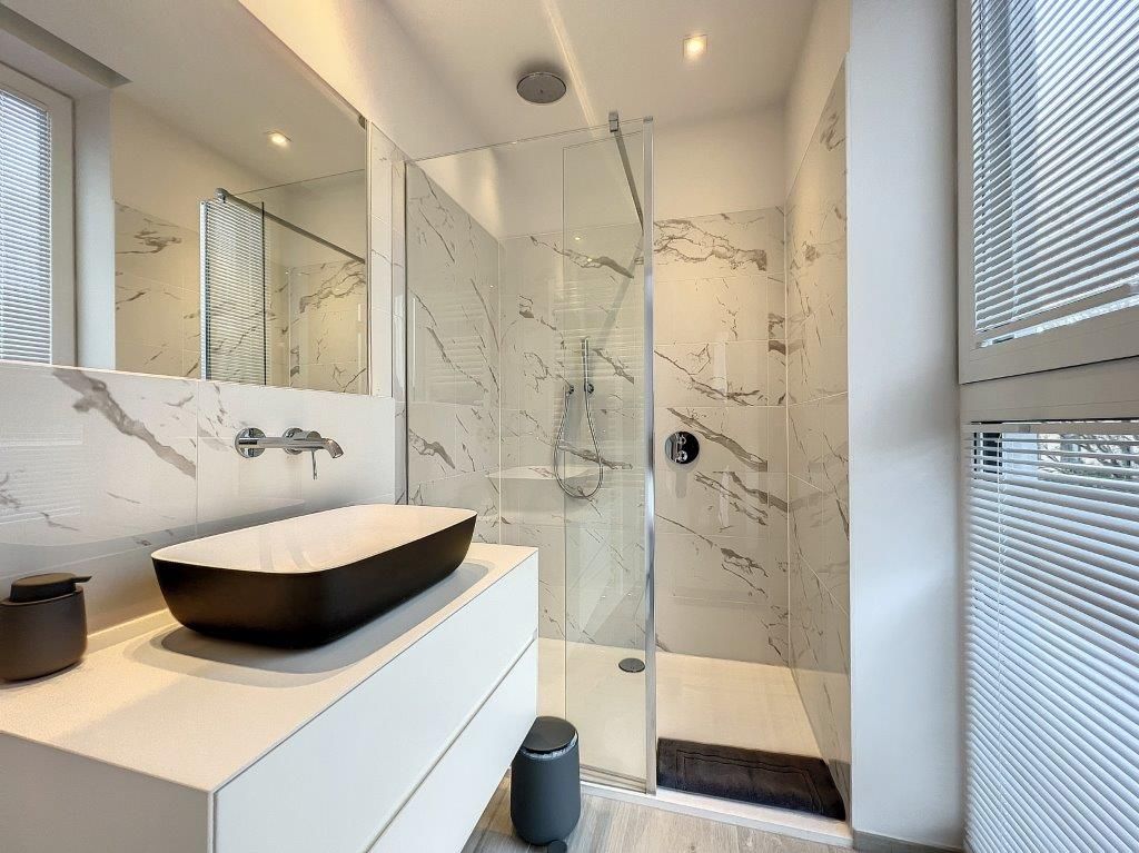 Salle de bain moderne en marbre clair, lavabo noir, douche à litalienne et ambiance élégante