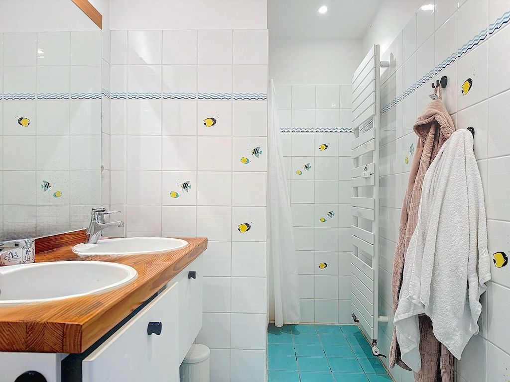 Salle de bain moderne lumineuse avec double lavabo en bois, douche en verre et accents jaunes.