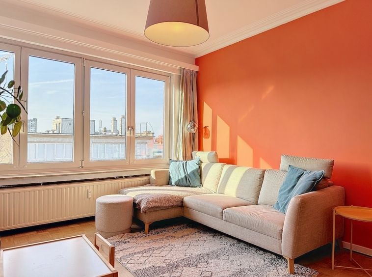 Salon moderne avec mur orange, canapé confortable, meubles en bois clair et décoration végétale.