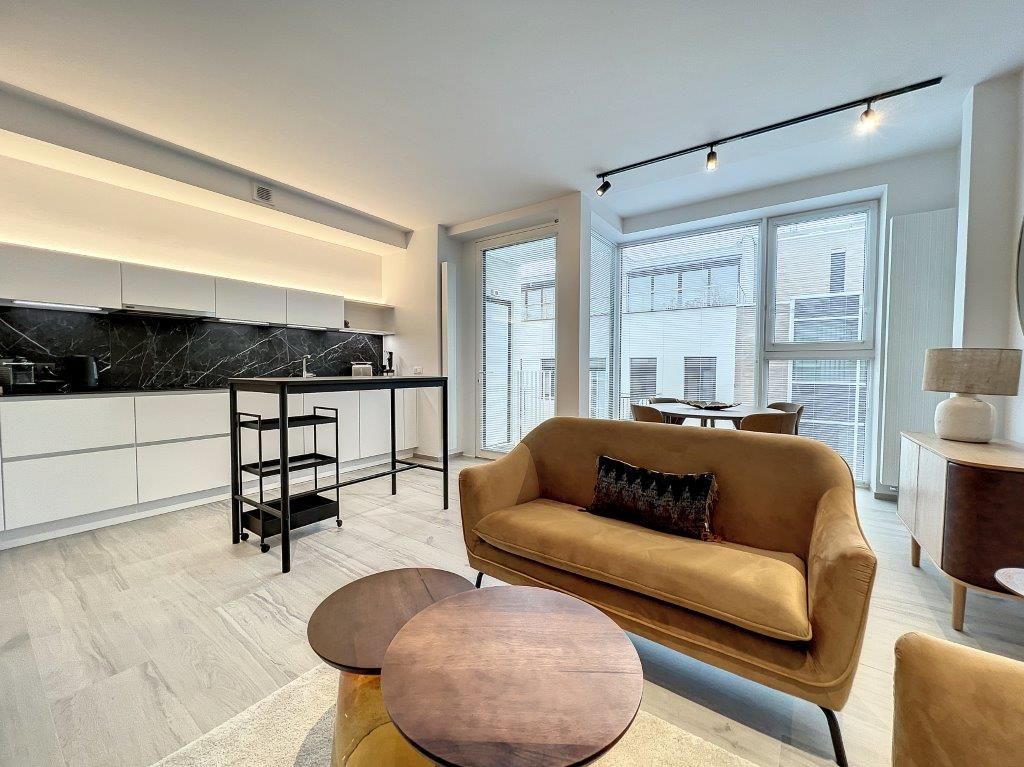Salon contemporain avec cuisine ouverte, lumière naturelle, mobilier élégant et ambiance chaleureuse.