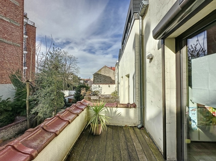 Balcon cosy avec vue sur jardin urbain, sol en bois, tuiles rouges et lumière naturelle.