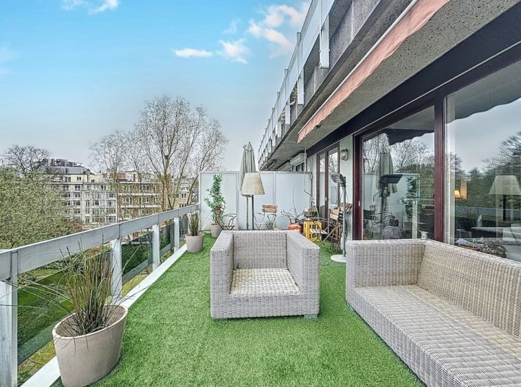 Balcon moderne avec gazon artificiel, fauteuils en rotin, vue dégagée, ambiance conviviale et élégante.