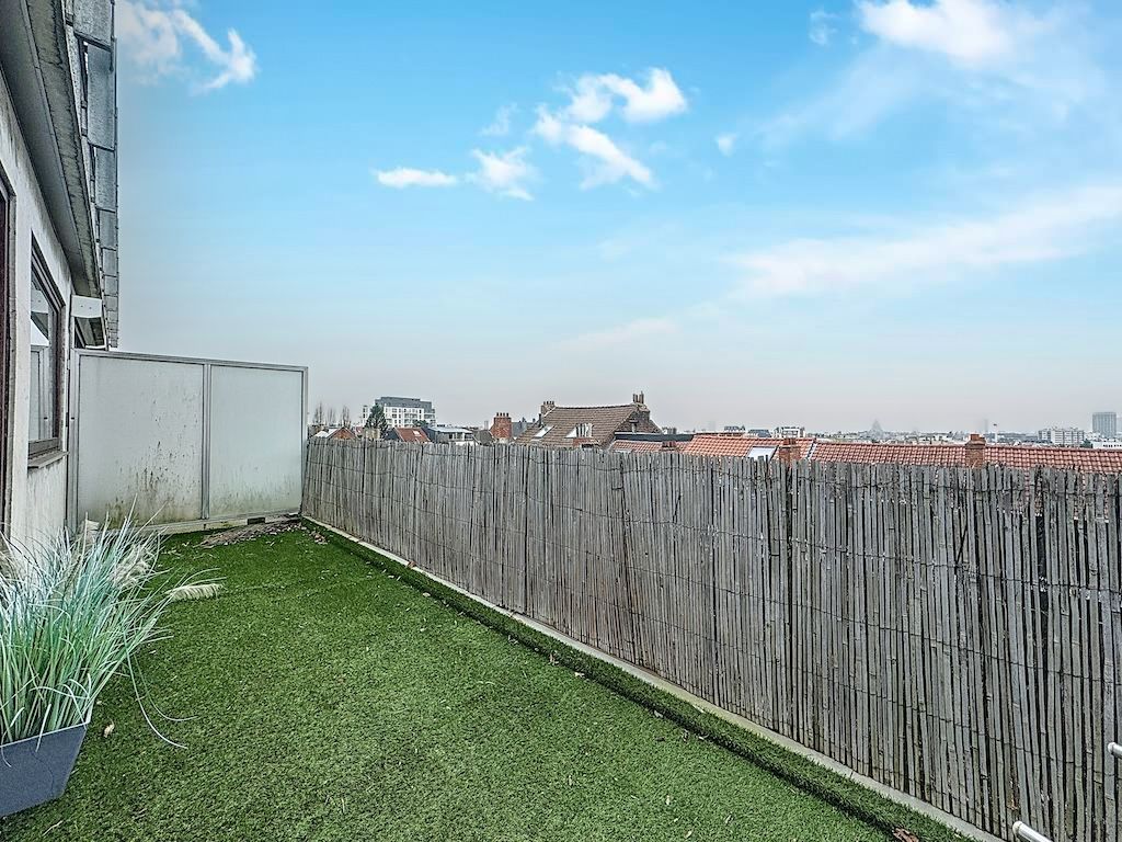 Balcon urbain avec pelouse artificielle, clôture en bambou et vue panoramique sur la ville.