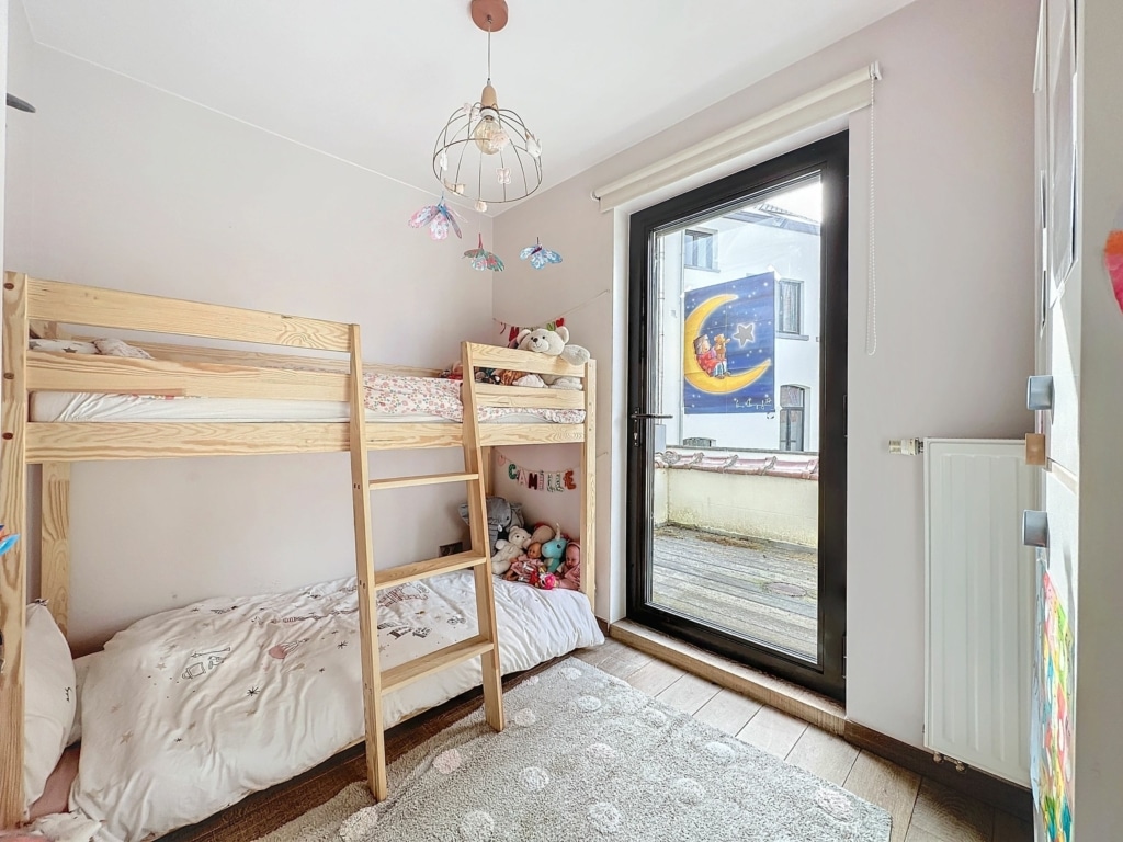 Chambre denfant chaleureuse avec lit superposé, décor coloré et grande fenêtre lumineuse.