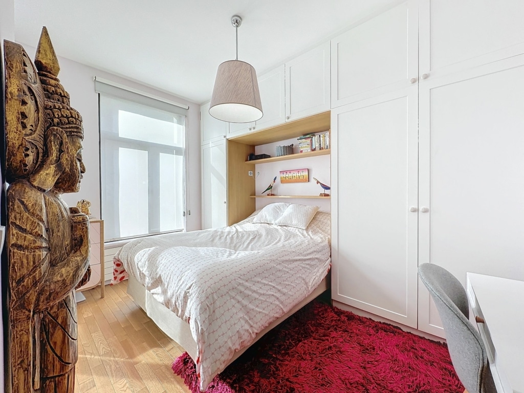 Chambre zen moderne avec statue Bouddha, lit blanc, tapis fuchsia et lumière naturelle.