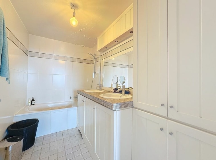 Salle de bain moderne blanche, double lavabo, baignoire, miroir large, rangements élégants, ambiance épurée.