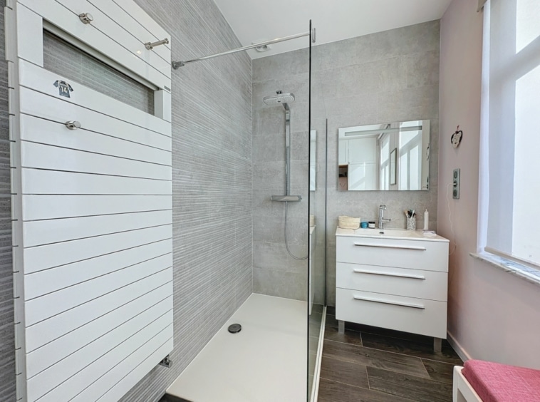Salle de bain moderne avec douche en verre, mobilier minimaliste et touche de couleur rose.
