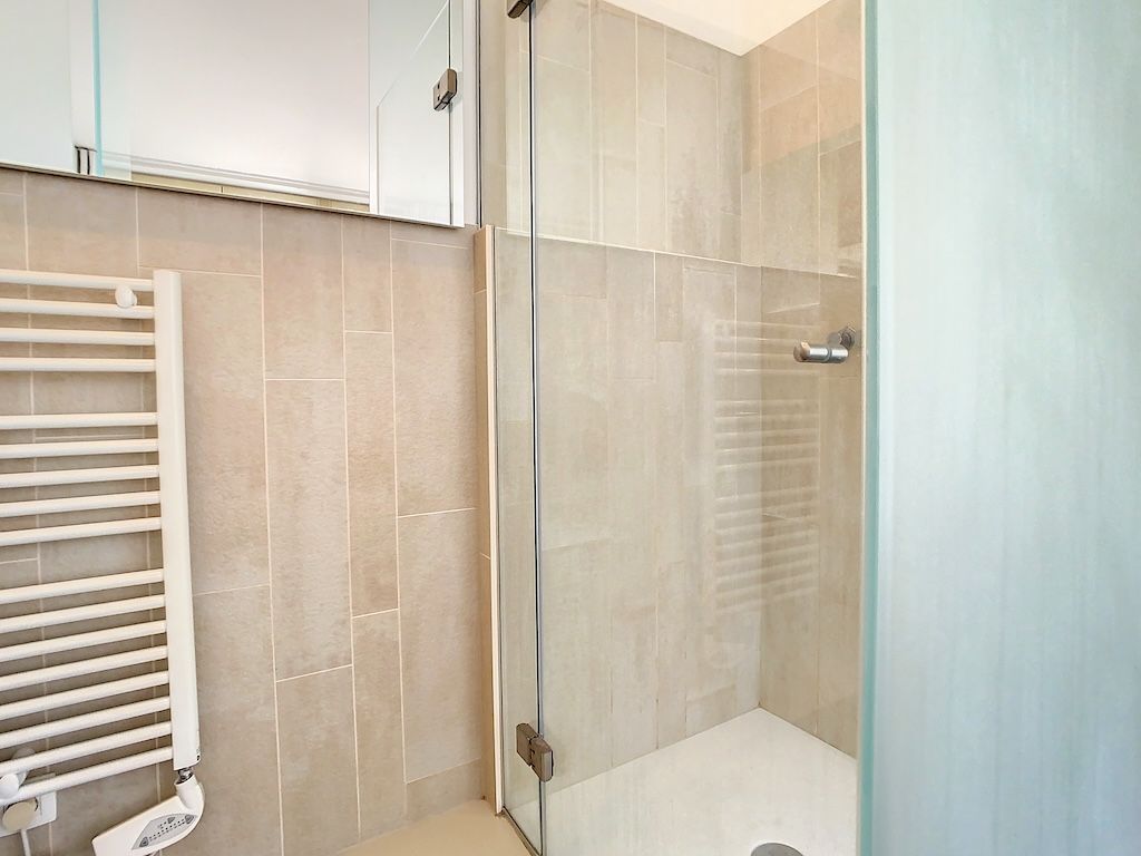 Salle de bain moderne minimaliste avec douche en verre, miroir et radiateur électrique design.