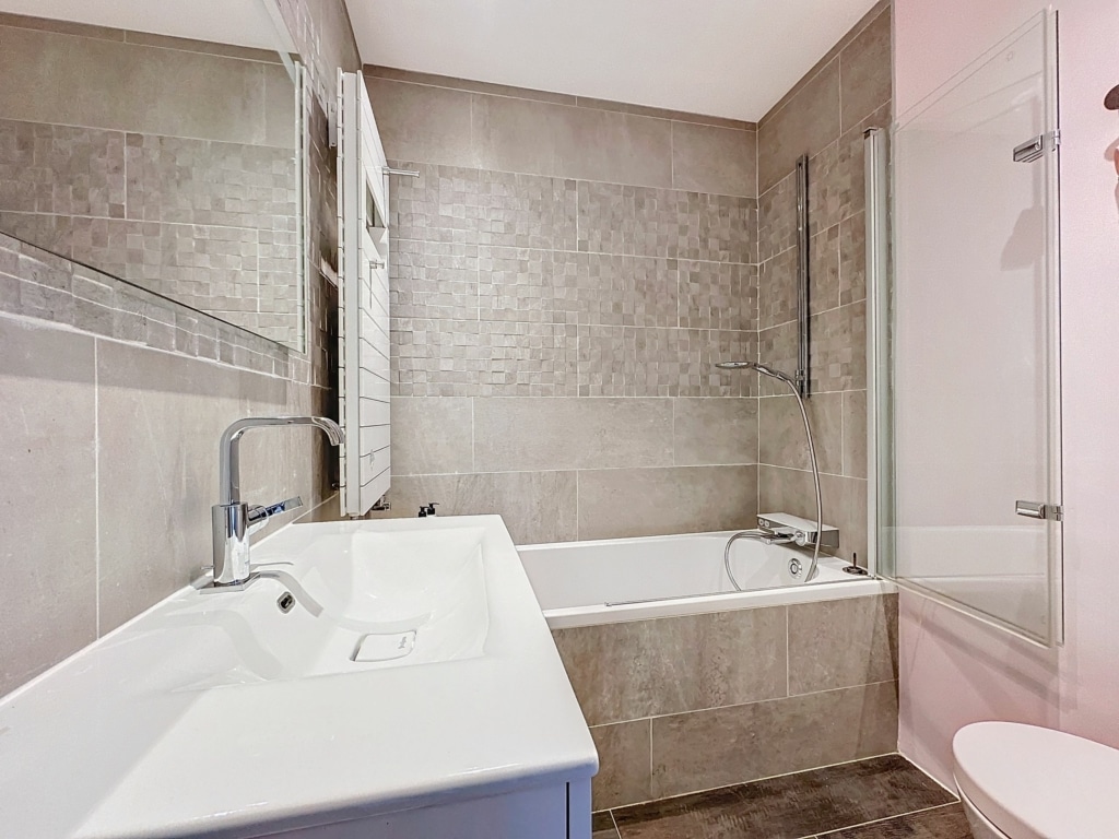 Salle de bain moderne avec baignoire, douche en verre, lavabo spacieux et design neutre élégant.