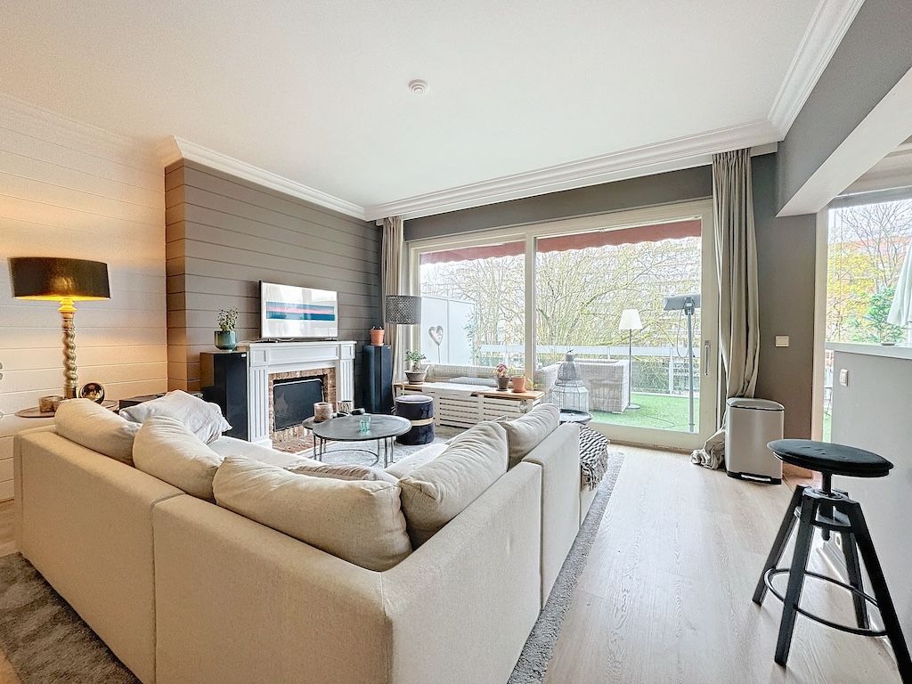 Salon moderne lumineux avec canapé cosy, table en verre, décoration épurée et vue verdoyante.
