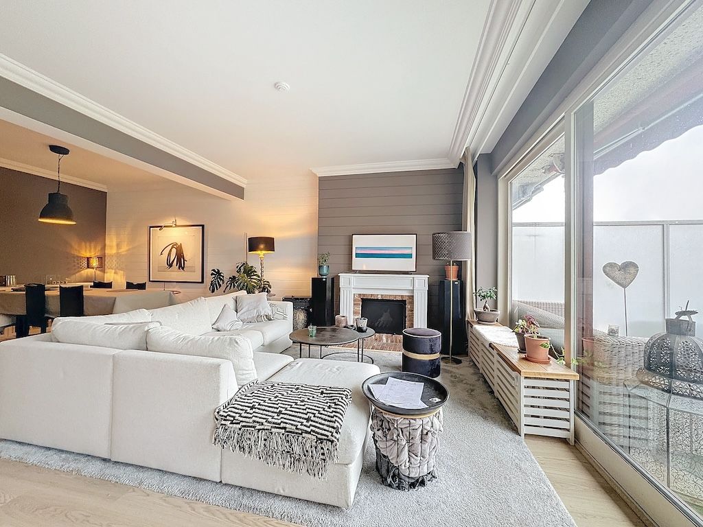 Salon moderne avec canapé blanc, cheminée, plantes, éclairage doux et œuvres colorées.