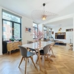 Salon moderne lumineux avec grande table en bois, vue sur la nature et décoration élégante.
