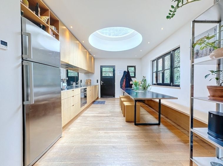 Cuisine moderne lumineuse avec matériaux chaleureux, puits de lumière circulaire et décoration végétale.