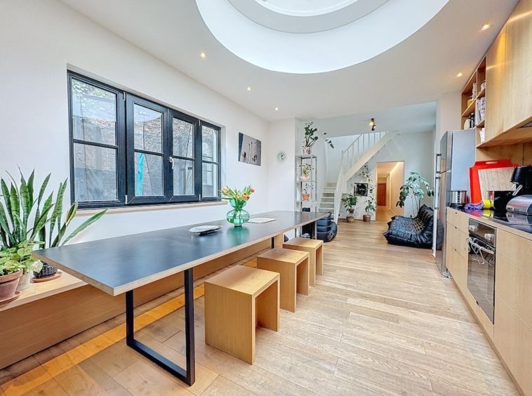 Cuisine moderne lumineuse avec plan noir, mobilier en bois, grandes fenêtres et puits de lumière circulaire.