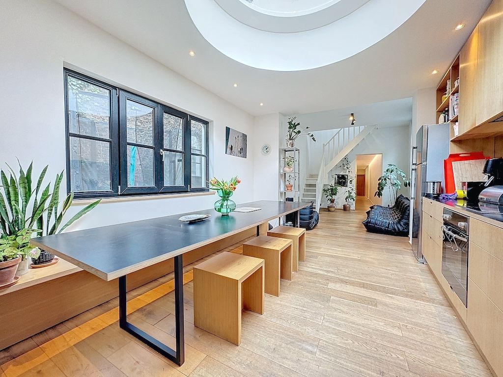 Cuisine moderne lumineuse avec plan noir, mobilier en bois, grandes fenêtres et puits de lumière circulaire.