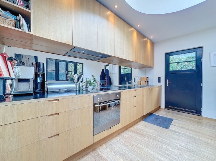 Cuisine moderne lumineuse avec meubles en bois clair, appareils intégrés et grande ouverture naturelle.