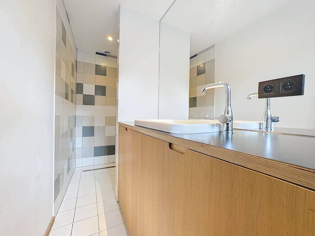 Salle de bains moderne minimaliste avec meuble en bois, carrelage pastel et miroir large.