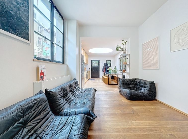 Espace moderne lumineux avec mobilier minimaliste, œuvres dart, plantes, et puits de lumière ronde.