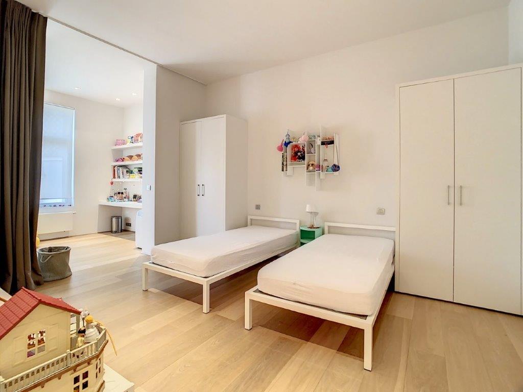 Chambre d’enfant minimaliste avec lits blancs, armoire moderne, lampe verte et décoration colorée.