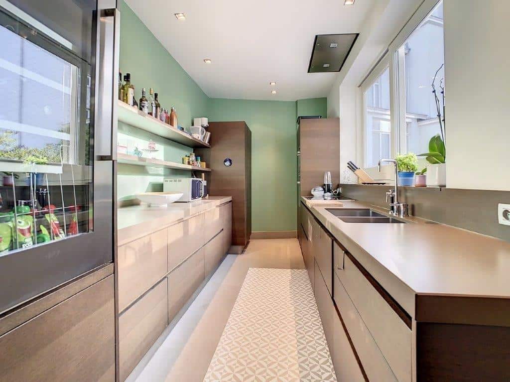Cuisine moderne avec murs verts, bois chaud, électroménagers intégrés et plantes naturelles