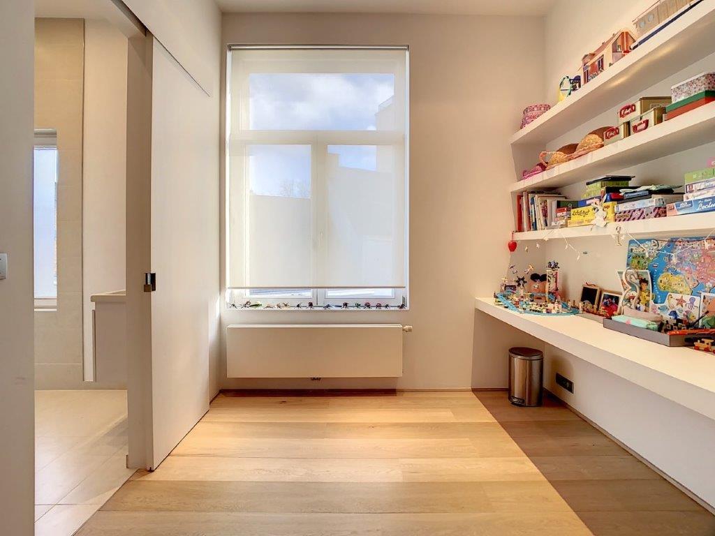 Espace de lecture minimaliste avec lumière naturelle, étagère éclectique, banquette près de la fenêtre.