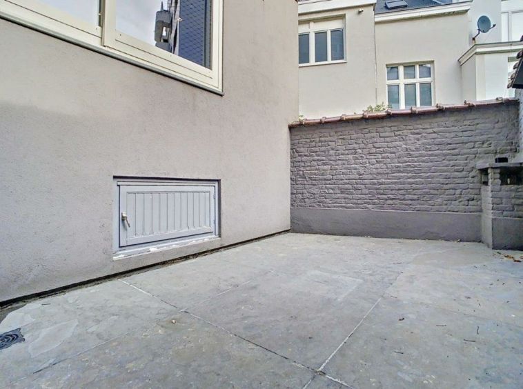 Espace urbain privé avec murs gris, fenêtre lumineuse et ambiance minimaliste.