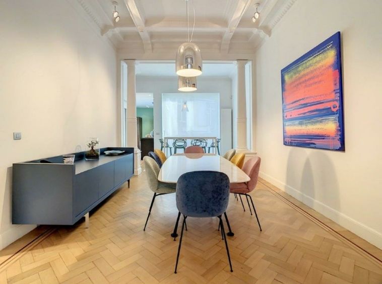 Salle à manger moderne avec parquet à chevrons, mobilier coloré et art dynamique.