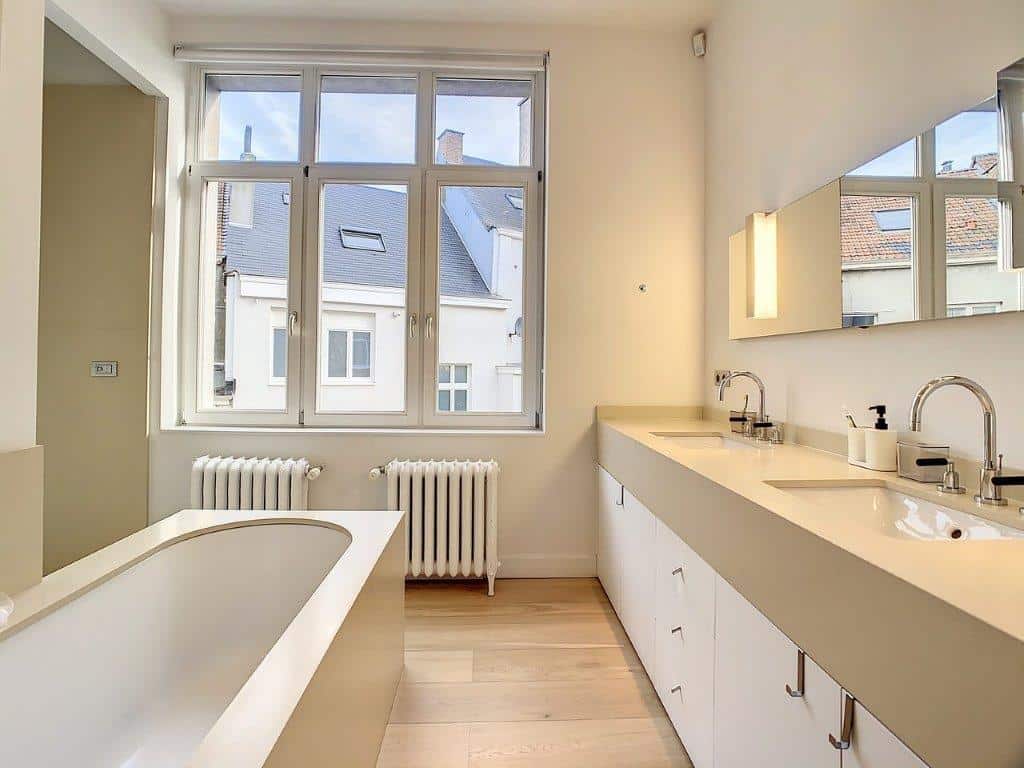 Salle de bain moderne avec baignoire, double vasques et vue urbaine naturelle.