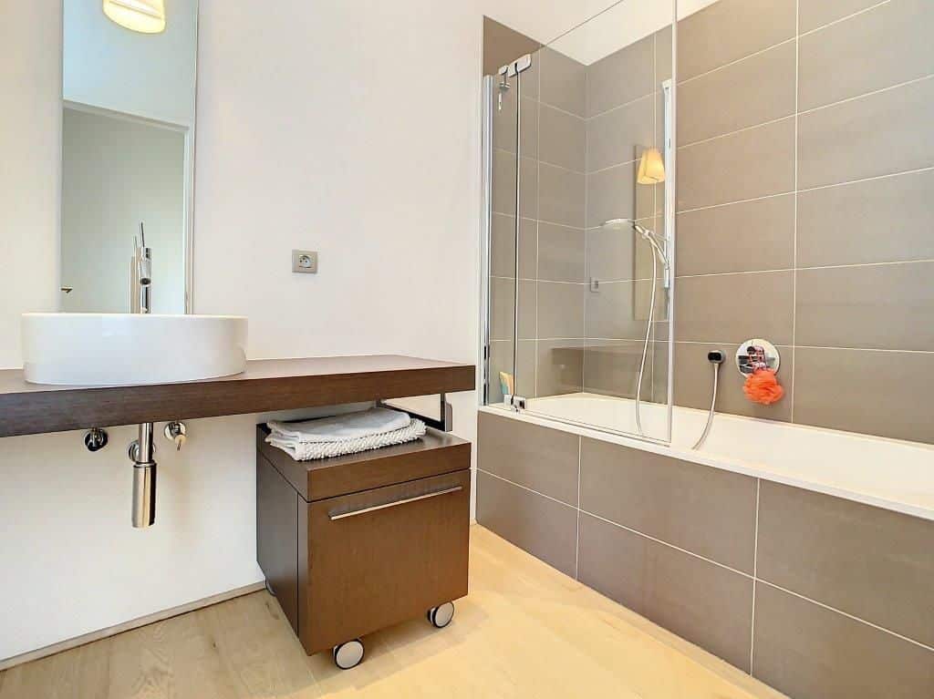 Salle de bain moderne, lumineuse, avec lavabo en bois, douche en verre et décoration épurée.