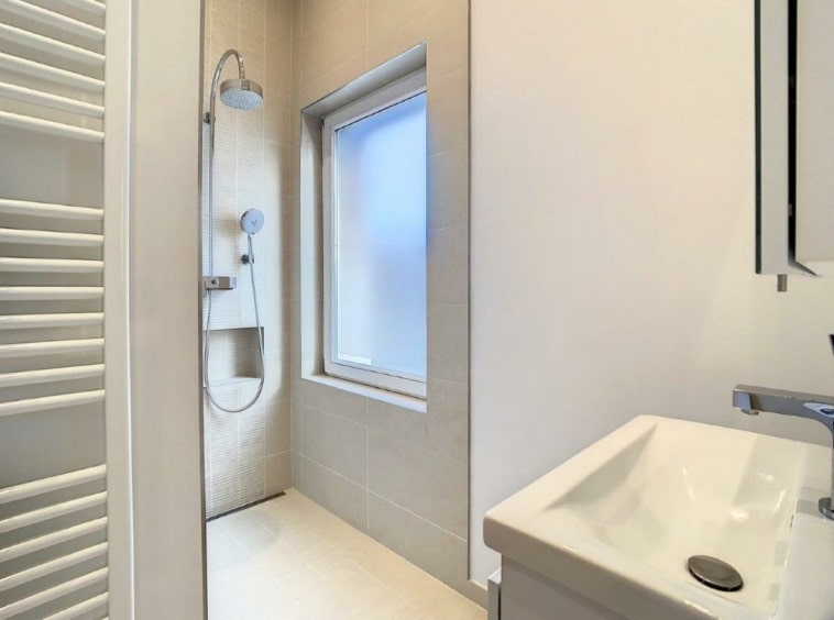 Salle de bain moderne avec douche pluie, lavabo minimaliste et radiateur-towel élégant.