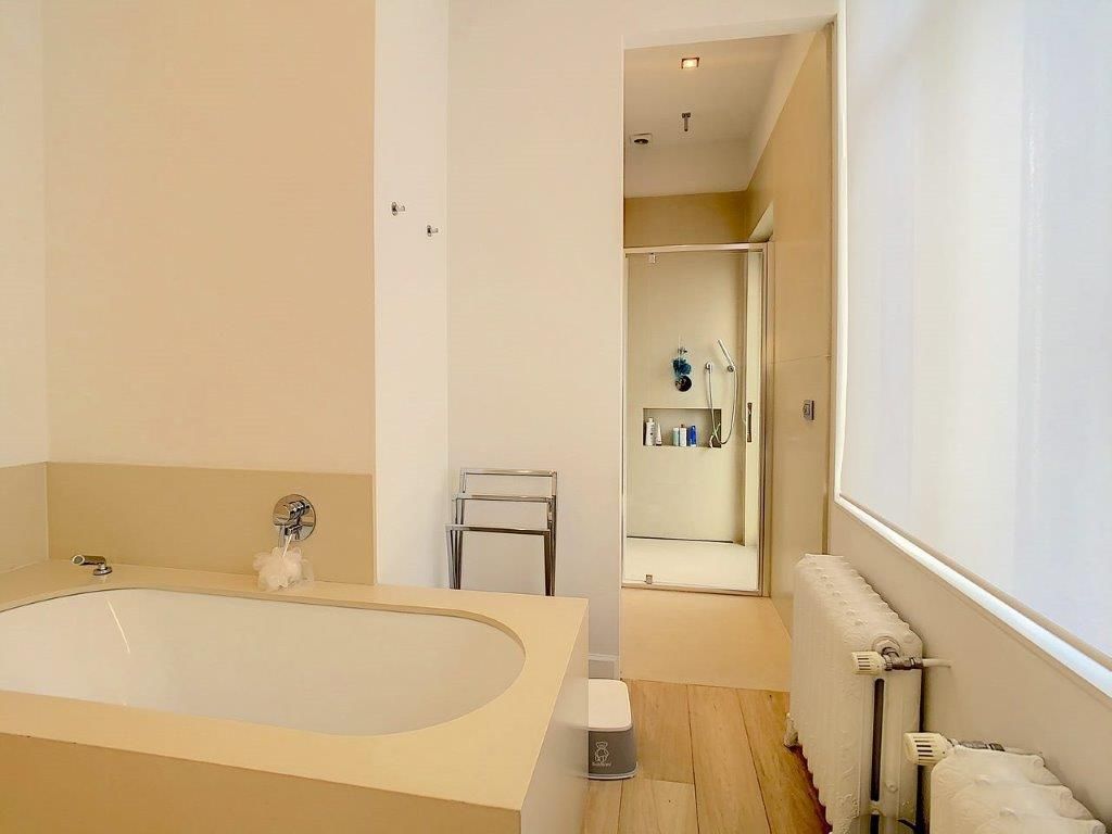 Salle de bain minimaliste avec baignoire autoportante, éclairage naturel, tons neutres et sol en bois.