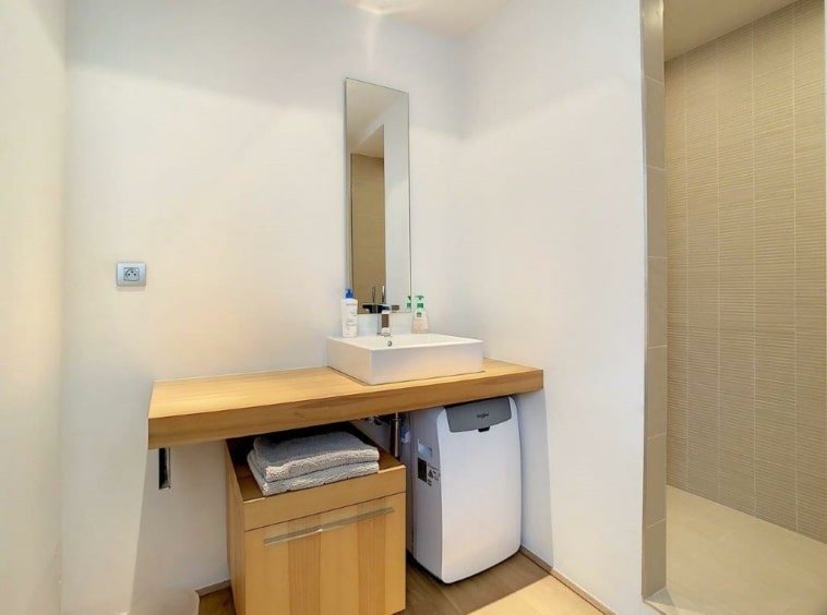 Salle de bain moderne minimaliste avec bois, lumière naturelle, douche en verre, espace épuré.