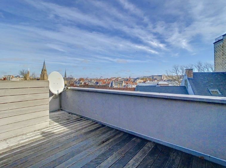 Terrasse urbaine en bois avec vue panoramique, antenne satellite, ciel bleu et paysages mêlés.