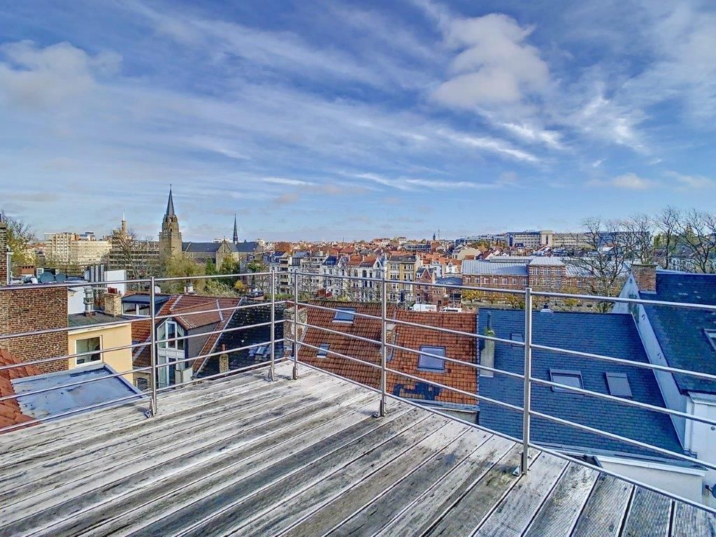 Vue sur la ville depuis un rooftop en bois, ciel bleu et architecture variée.