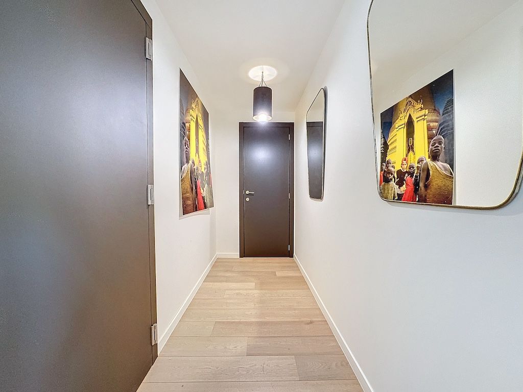 Couloir moderne lumineux avec miroir, œuvres dart colorées, porte sombre et éclairage contemporain.