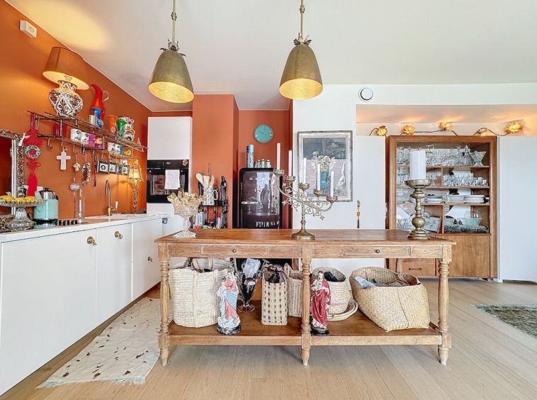 Cuisine chaleureuse et éclectique avec îlot en bois, murs orange, décor coloré et éclairage doux.